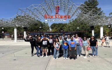 Grupo de alumnos, profesores y familias de iQ Academy posando juntos frente a la entrada de Six Flags Magic Mountain en un día soleado.