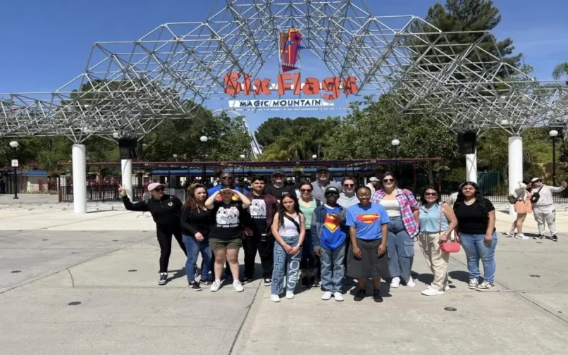 Grupo de alumnos, profesores y familias de iQ Academy posando juntos frente a la entrada de Six Flags Magic Mountain en un día soleado.